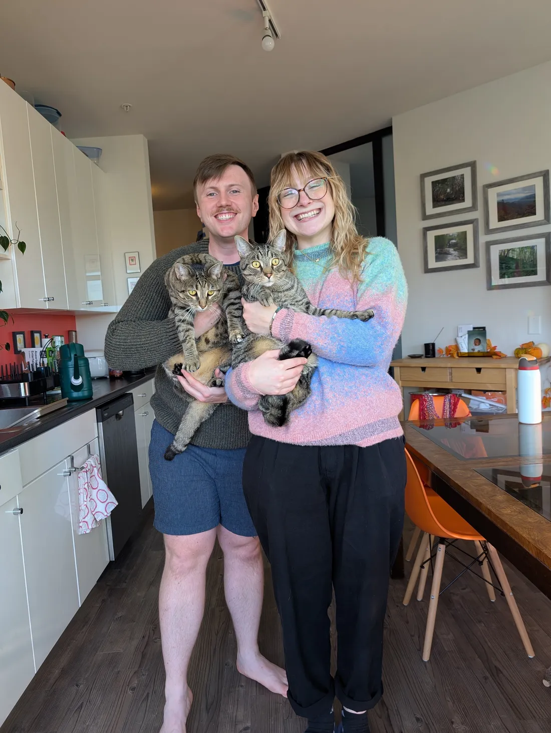 Cat and Zach in their kitchen, each holding one of their tabby cats.